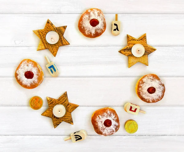 Wooden candlesticks in the shape of star, donuts, golden chocolate coins and wooden dreidels on background of white painted wooden with space for text. Top view, flat lay