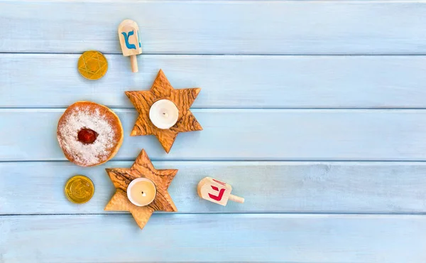 Wooden candlesticks in the shape of star, donut, golden chocolate coins and dreidels on background of blue painted wooden planks with space for text. Top view, flat lay