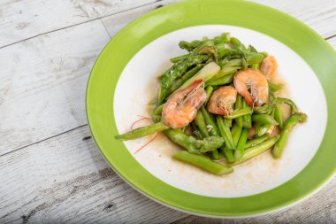 Kızarmış kuşkonmaz, karides, Asya sokak yemeği, ahşap bir zeminde yeşil bir sınır çanağı, sokak yemeği. Fotoğraf.