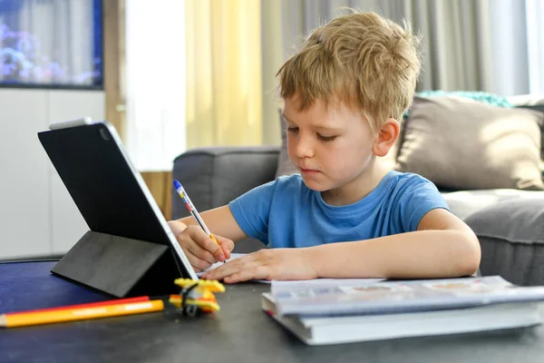 Home schooling, on-line education. A kid studing on-line, doing homework with his gadget.