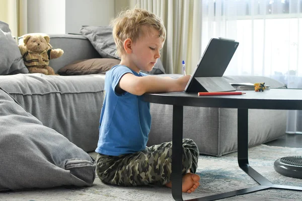 Home schooling, on-line education. A kid studing on-line, doing homework with his gadget.