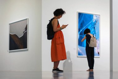 Moskova 11 / 06 / 2019 Fotoğraf sergisindeki insanların davranışları - bir kadın duvardaki resmi inceliyor, diğeri cep telefonundaki sosyal ağ iletişimi tarafından özümseniyor, çevresindeki hiçbir şeye dikkat etmiyor