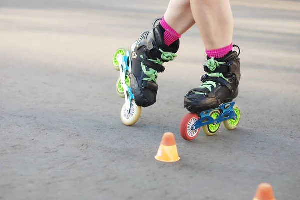 roller skater legs in motion, inline roller skating, rollerblading, slalom on asphalt surface. Small cones for training on the road.