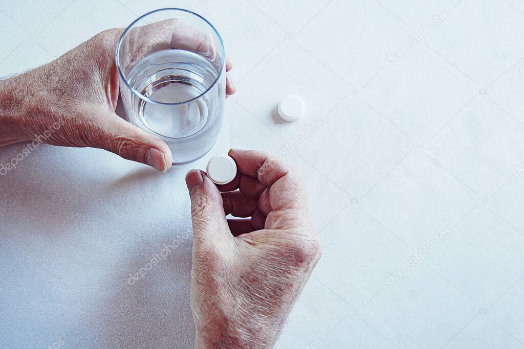 Elderly man hands taking medicine pill with a glass of water