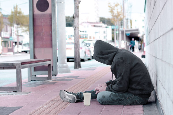 Бедный бездомный или беженец спит на деревянной скамейке на тротуаре в городе