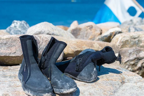 Dive boots drying on a stone. A dive flag and blue water in the background — Stock Photo, Image