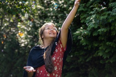 Sabun köpüğü kovalayan genç bir kız. Yeşil yapraklar arkaplan