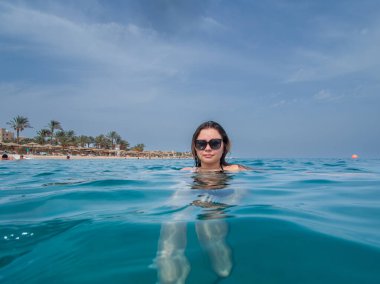 A young woman with sun glasses swimming in the blue sea. A blue hazy sky in the background. Picture from the Red Sea, Egypt