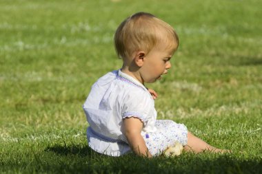 Küçük kız çimenlerde oturuyor.