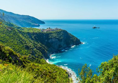 Yaz mevsiminde İtalya 'nın Corniglia kentindeki tepedeki köye bir helikopter yaklaşıyor.