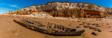Old Hunstanton Sahili 'nin geniş açılı görüntüsü bir gemi enkazı, tebeşir taşları ve Norfolk, İngiltere' deki beyaz, kırmızı ve turuncu katmanlı uçurumları gösteriyor.