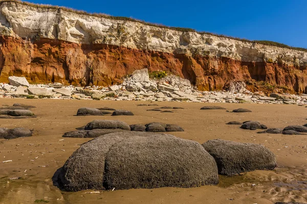 Denizi aşındıran bir manzara tebeşirle kayalara doğru kayaları aşındırdı. Old Hunstanton, Norfolk, İngiltere 'deki beyaz, kırmızı ve turuncu katmanlı uçurumların dibine düştü.