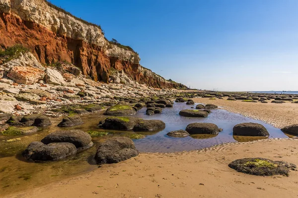 Old Hunstanton, Norfolk, İngiltere 'deki beyaz, kırmızı ve turuncu katmanlı kayalıkların tabanındaki kayalar ve kaya havuzları
