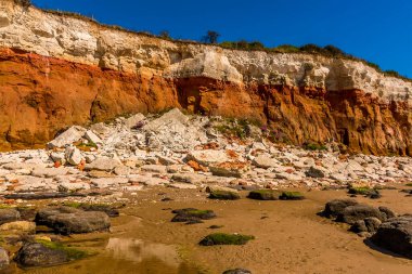 Old Hunstanton, Norfolk, İngiltere 'deki beyaz, kırmızı ve turuncu katmanlı kayalıklardan büyük bir kaya düşüşü.