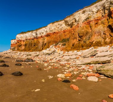 Yaşlı Hunstanton, Norfolk, İngiltere 'deki beyaz, kırmızı ve turuncu katmanlı kayalıkların eteklerindeki beyaz ve turuncu kayalıklar kumsalı kirletir.