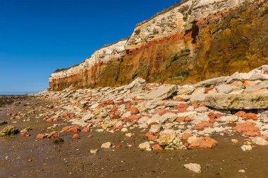 Old Hunstanton plajındaki kayalar, Norfolk, İngiltere 'deki beyaz, kırmızı ve turuncu katmanlı kayalıklarda bulunan üçlü katmanları yansıtıyor.