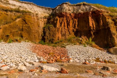 Doğal olarak kırmızı ve beyaz kayalar beyaz, kırmızı ve turuncu katmanlı uçurumlardan Norfolk, İngiltere 'deki Old Hunstanton deniz duvarına doğru ayrılıyor.