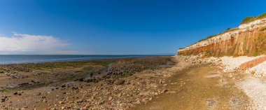 Sahilin karşısında ve Old Hunstanton, Norfolk, İngiltere 'deki beyaz, kırmızı ve turuncu katmanlı uçurumlar boyunca bir manzara.
