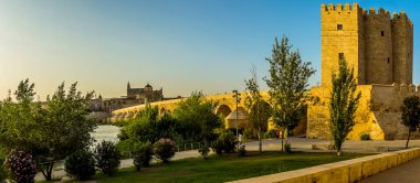 Parkın karşısındaki günbatımına doğru bakan Roma köprüsü ve İspanya 'nın Cordoba şehrinde yazın aydınlanan