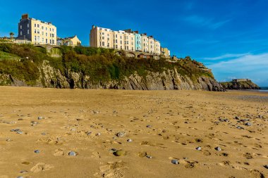 Güneşli bir günde Tenby 'deki kayalıklara ve renkli otellere bakan Güney Sahili' ndeki kum ve çakıl taşlarının manzarası