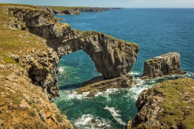 Yazın başında Castlemartin yakınlarında, Pembrokeshire 'in güney batı kıyısındaki Yeşil Galler Köprüsü ve kaya sütunları adı verilen dramatik bir doğal kaya kemeri.
