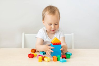 2 yaşında bir çocuk beyaz izole bir arka planda bir masada oturuyor ve bir inşaatçı topluyor, erken gelişim, bir metin yeri.