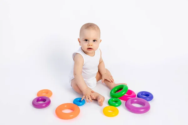 可爱的小孩 8个月大 身穿白色紧身衣 与发展中的玩具玩耍 坐在白色的背景上 为文字留出空间 — 图库照片