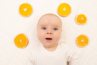 Beyaz arka planda portakallı bir bebek portresi. Çocuklar için yatak. 8 aydır. Vücut pijamalı sağlıklı bir çocuk. Çocuklarda Citrus alerjisi