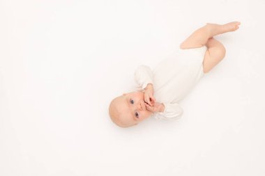 Beyaz elbiseli güzel bir kız çocuğu beyaz bir arka planda kameraya bakıyor, 3 aylık bebek yatakta yatıyor, mesaj için yer var.