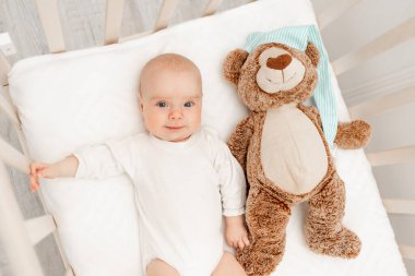 Uyuyan bebek ve beyaz beşikteki oyuncağı. Çocuk yuvası ve çocuklar için yatak. Beşikte şekerleme yapan şirin bir çocuk. Çocuk beyaz yatak odasında kestiriyor. Vücut pijamalı sağlıklı bir çocuk..
