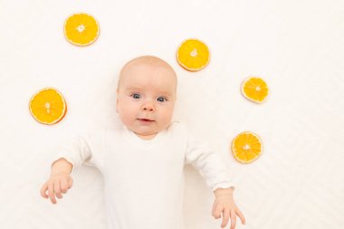 Beyaz arka planda portakallı bir bebek portresi. Çocuklar için yatak. 8 aydır. Vücut pijamalı sağlıklı bir çocuk. Çocuklarda Citrus alerjisi