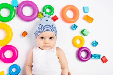 Ringin oyuncakları arasında beyaz arka planda yatan küçük bir çocuk. Metin için boşluk. Erken gelişme