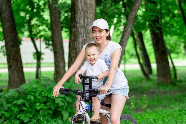 mother and son ride a Bicycle, mother carries a child in a child\'s chair on a Bicycle in the Park in the summer