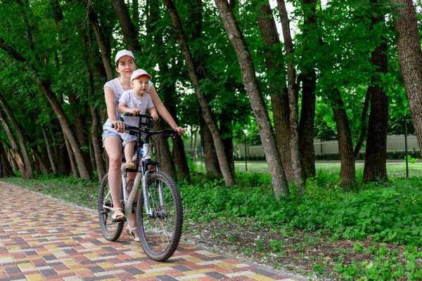 mother and son ride a Bicycle, mother carries a child in a child\'s chair on a Bicycle in the Park in the summer