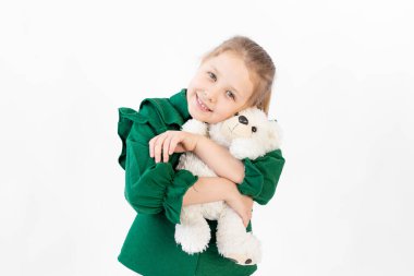 Yeşil elbiseli şirin küçük bir kız oyuncak ayıya sarılıyor, mesaj için yer var, 8 yaşında.