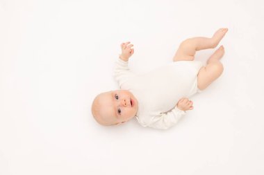 Beyaz elbiseli güzel bir kız çocuğu beyaz bir arka planda kameraya bakıyor, 3 aylık bebek yatakta yatıyor, mesaj için yer var.