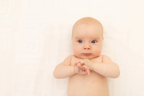 cute baby girl in a white bodysuit on a white isolated background looking at the camera, baby 3 months old lying on the bed, space for text