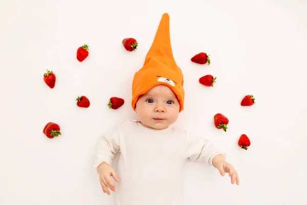 cute girl in a white bodysuit on a white isolated background eating a strawberry, first feeding, baby 3-6 months among berries, Allergy to berries, fruit, space for text. Healthy child.