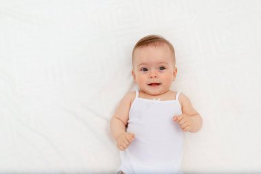Gülümseyen bir kızın portresi. 6 aylık bir bebek beşikte sırtüstü uzanmış, kameraya bakıyor, bebek sabahları, çocuk eşyaları konsepti.