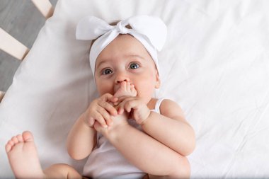 Bebek 6 aylık bebek beşikte yatıyor, sırtında beyaz elbiseler ve gülüyor, kameraya bakıyor, bebek ürünleri konsepti.