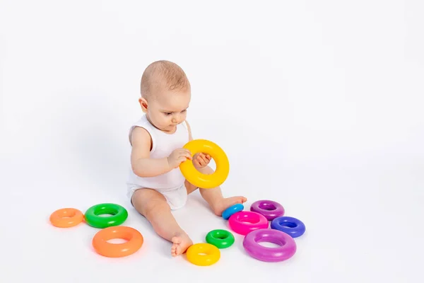 可爱的小孩 8个月大 身穿白色紧身衣 与发展中的玩具玩耍 坐在白色的背景上 为文字留出空间 — 图库照片