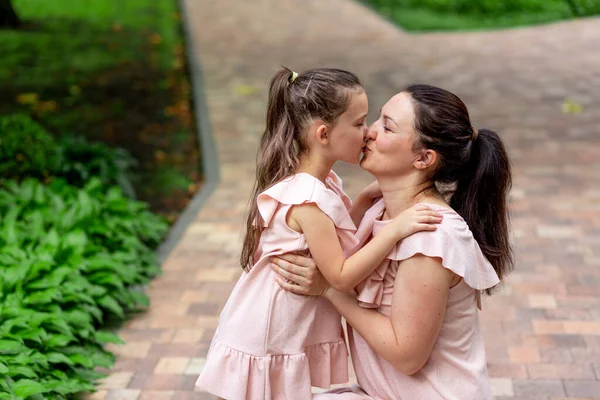 Happy mother and daughter 5-6 years old walk in the Park in the summer, mother kisses her daughter, the concept of a happy family, the relationship of mother and child.