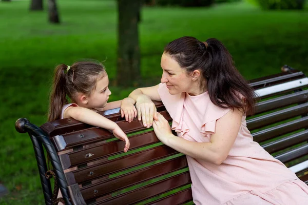 mother and daughter 5-6 years old walking in the Park in the summer, mother talking to her daughter sitting on a bench, the concept of a happy family, the relationship of mother and child, mother's day.