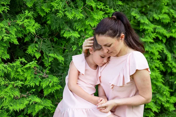 mother hugs daughter 5-6 years old sitting in the Park on the grass, mother-daughter conversation, mother feels sorry for the child, mother-child relationship, mother\'s Day