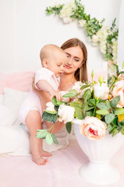 Genç ve güzel bir anne kızını kucağına alır. Beyaz bir yatakta 6 aylık bir kız. Çiçeklere bakar.