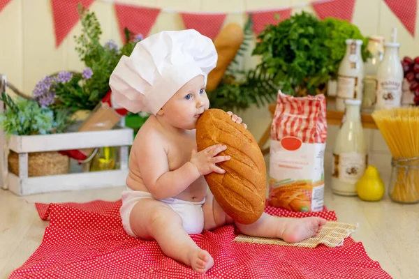 a baby in a cook\'s hat sits back in a beautiful photo zone with flour and vegetables, a cook\'s child, a child with flour and bread prepares food