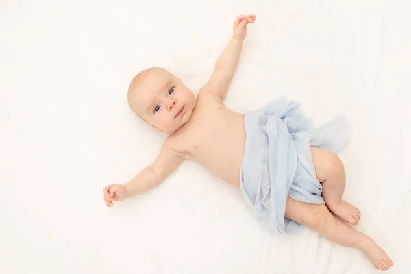 cute baby girl in a white bodysuit on a white isolated background looking at the camera, baby 3 months old lying on the bed, space for text