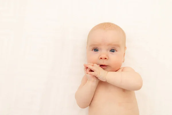 cute baby girl in a white bodysuit on a white isolated background looking at the camera, baby 3 months old lying on the bed, space for text