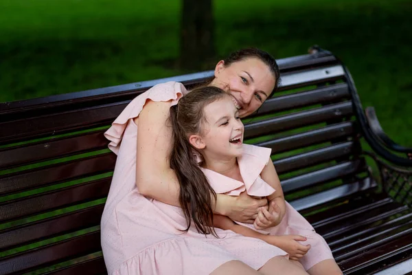 mother and daughter 5-6 years old walking in the Park in the summer, daughter and mother laughing on a bench, the concept of a happy family, the relationship of mother and child, mother\'s day
