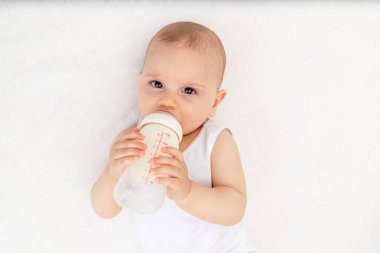 8 aylık erkek bebek, bebek odasında sırt üstü yatar ve elinde bir şişe süt tutar, bebeği besler, bebek maması konsepti yaratır.
